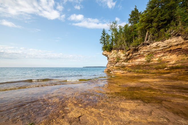 Rocky outcroppings define the Lake Superior shoreline of Pictured Rocks National Lakeshore in Munising, Michigan. Grand Island is shown in the distance.